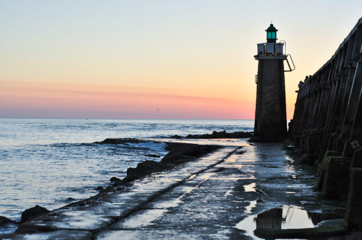 This sunset scene takes place at the Capbreton Lighthouse. You can see the reflection of the lighthouse in the puddle